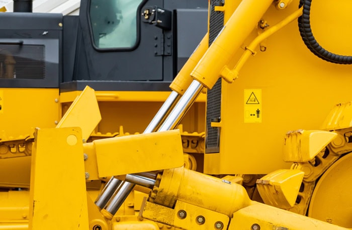 Close up hydraulic system of yellow bulldozer at industrial construction site, with mechanical cylinder and steel component for infrastructure and excavation work